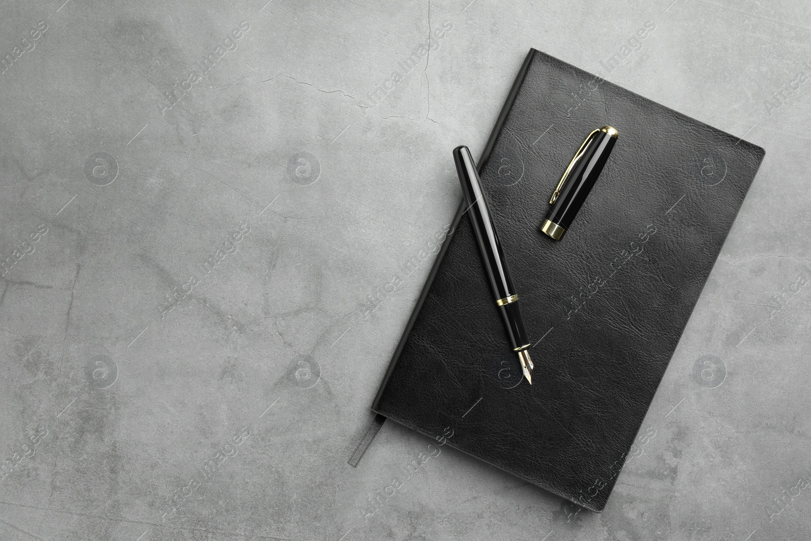 Photo of Stylish fountain pen, cap and notebook on light grey textured table, top view. Space for text