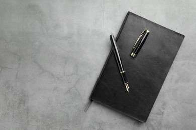 Photo of Stylish fountain pen, cap and notebook on light grey textured table, top view. Space for text