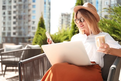 Photo of Beautiful woman with laptop and coffee using phone at outdoor cafe