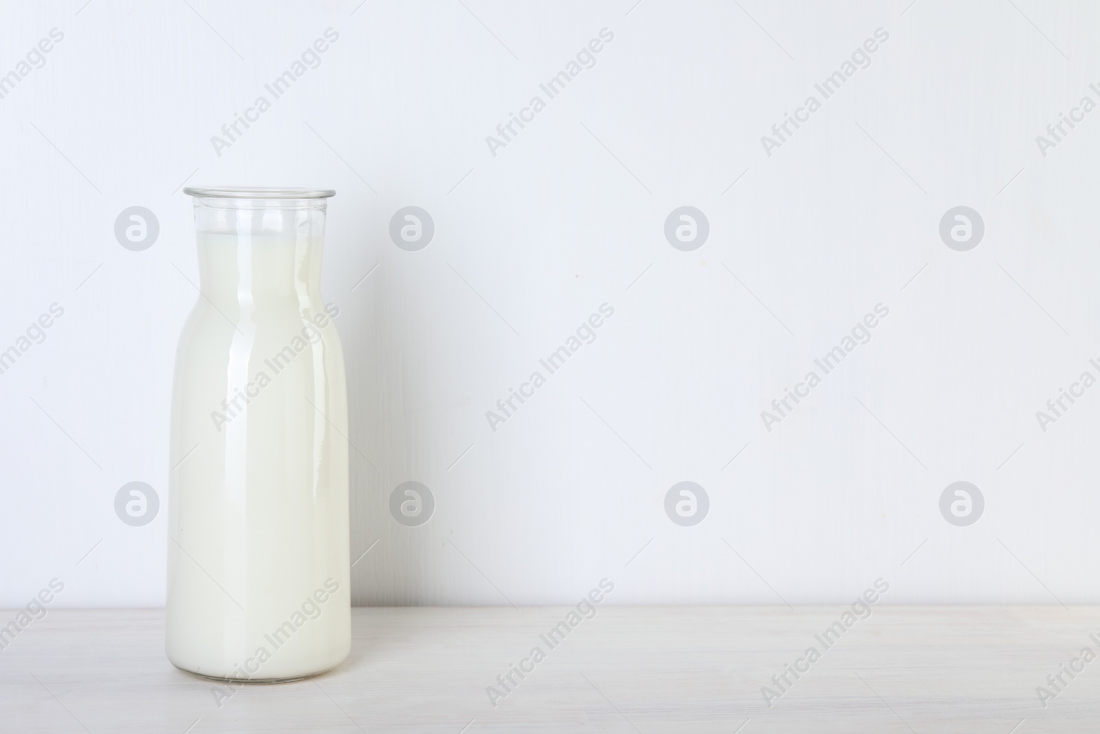 Photo of Glass carafe of fresh milk on wooden table, space for text