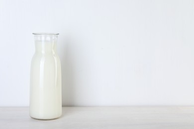 Photo of Glass carafe of fresh milk on wooden table, space for text