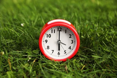 Photo of Red alarm clock on green grass outdoors
