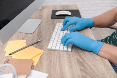 Photo of Office employee in latex gloves working with computer at wooden table, closeup