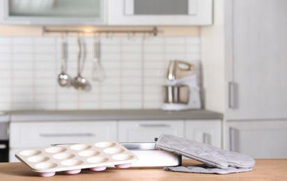 Photo of Clean baking dish, muffin pan and oven glove on table in kitchen. Space for text