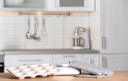 Clean baking dish, muffin pan and oven glove on table in kitchen. Space for text