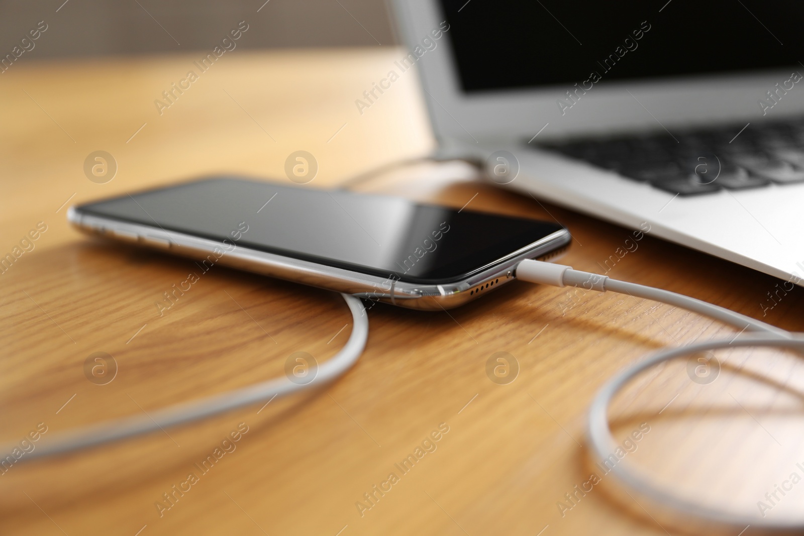 Photo of Modern smartphone charging from laptop on wooden table, closeup