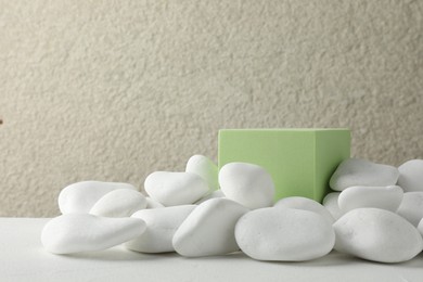 Photo of Presentation for product. Light green cube podium and white pebbles on table. Space for text