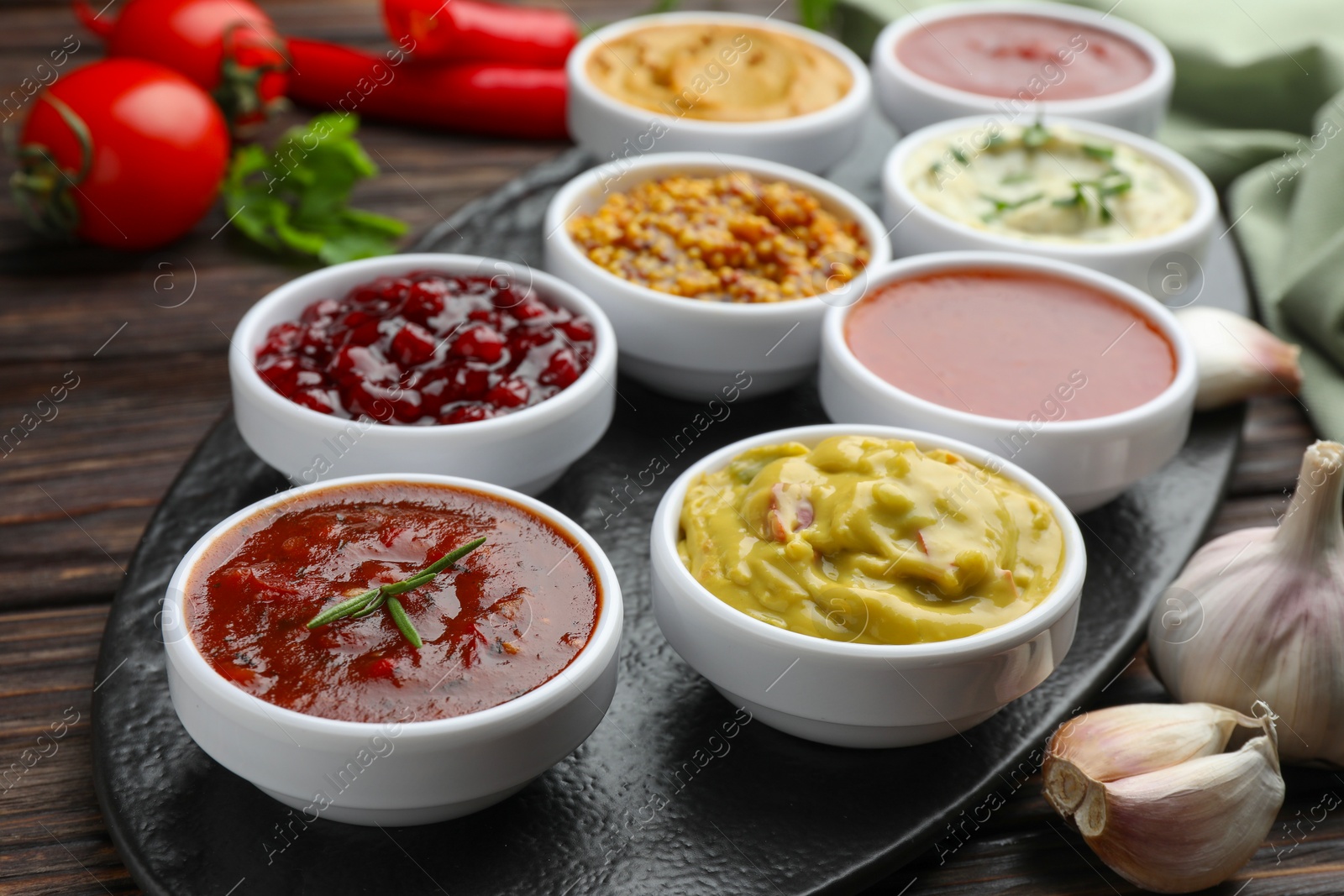 Photo of Different tasty sauces in bowls and garlic on wooden table, closeup