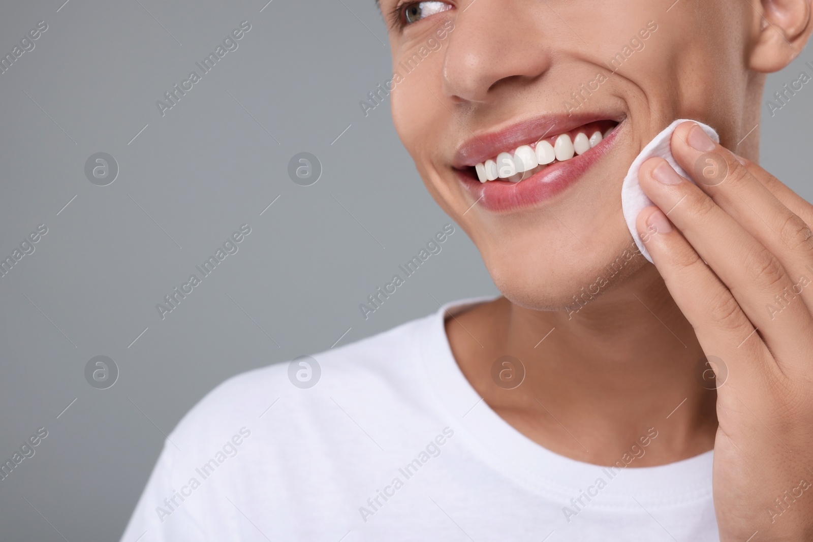 Photo of Man cleaning face with cotton pad on grey background, closeup