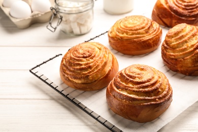 Photo of Cooling rack with tasty buns on white wooden table. Fresh from oven