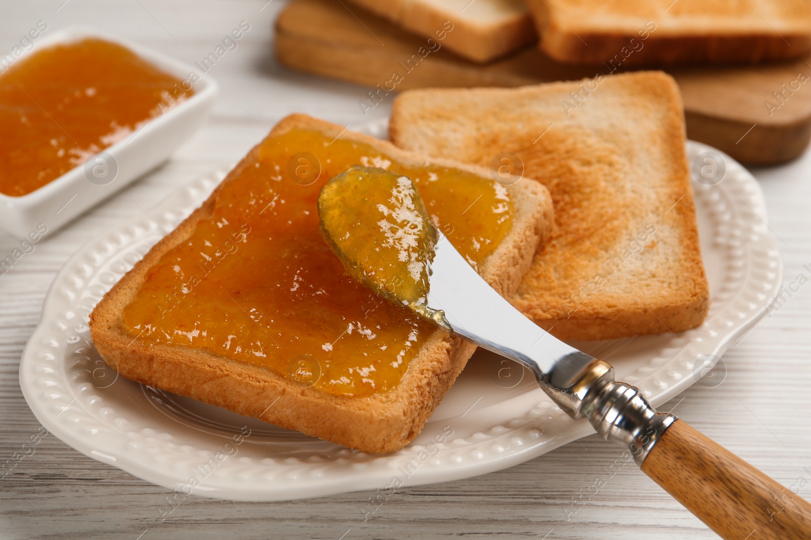 Photo of Toast with tasty orange jam, roasted slice of bread and knife on white wooden table, closeup