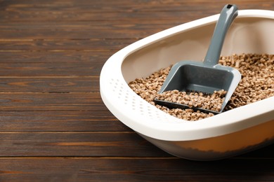 Photo of Cat litter tray with filler and scoop on wooden background, closeup. Space for text