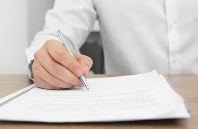 Man signing document at wooden table, closeup