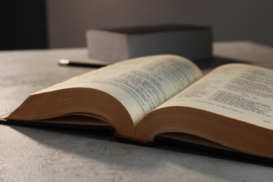 Photo of Closeup view of open hardcover Bible on grey table indoors. Religious book