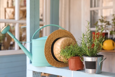 Photo of Potted plants, watering can and straw hat on light blue wooden veranda railing outdoors. Gardening tools