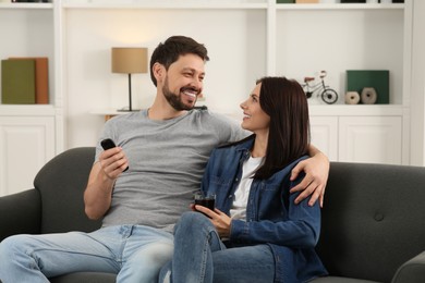 Photo of Happy couple spending time together at home. Man changing TV channels with remote control