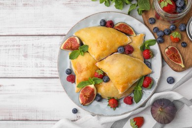 Delicious samosas with figs and berries on white wooden table, flat lay. Space for text