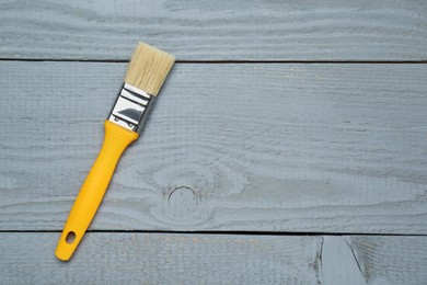 One paint brush with yellow handle on grey wooden table, top view. Space for text