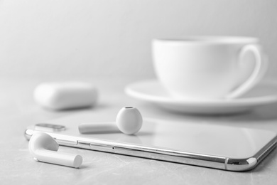 Photo of Modern wireless earphones and mobile phone on light table