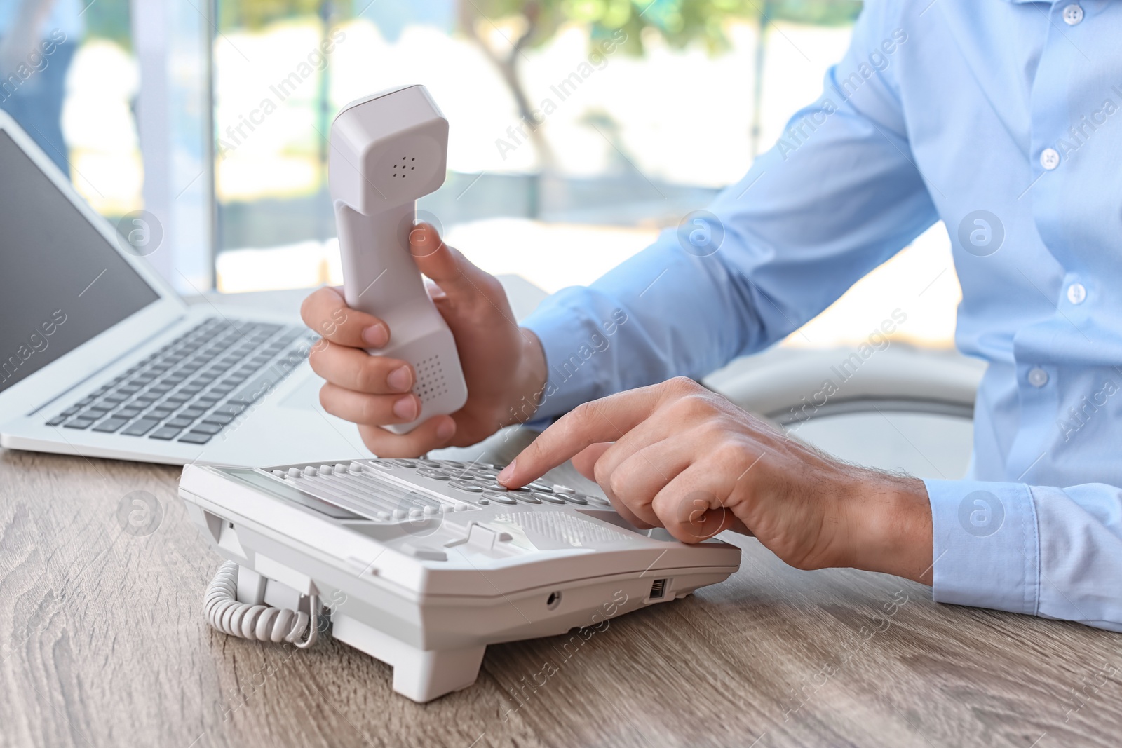 Photo of Man dialing number on telephone at workplace