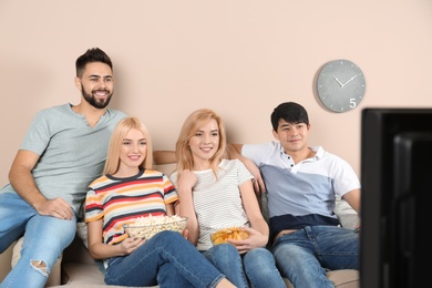 Photo of Young friends with snacks watching TV on sofa at home