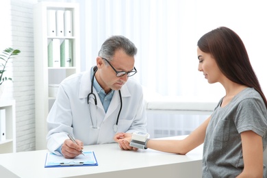 Doctor checking young woman's pulse with medical device in hospital