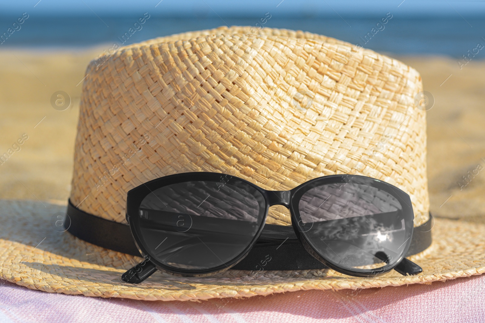 Photo of Hat with beautiful sunglasses on blanket near sea, closeup