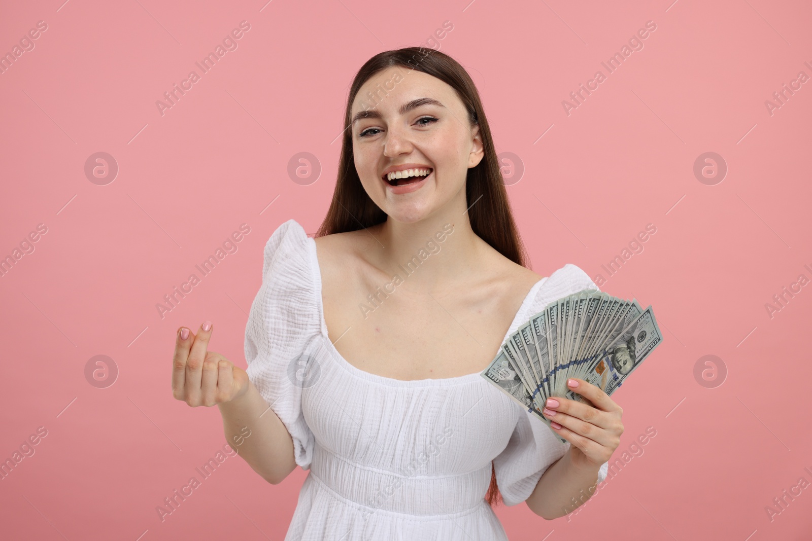 Photo of Happy woman with dollar banknotes showing money gesture on pink background