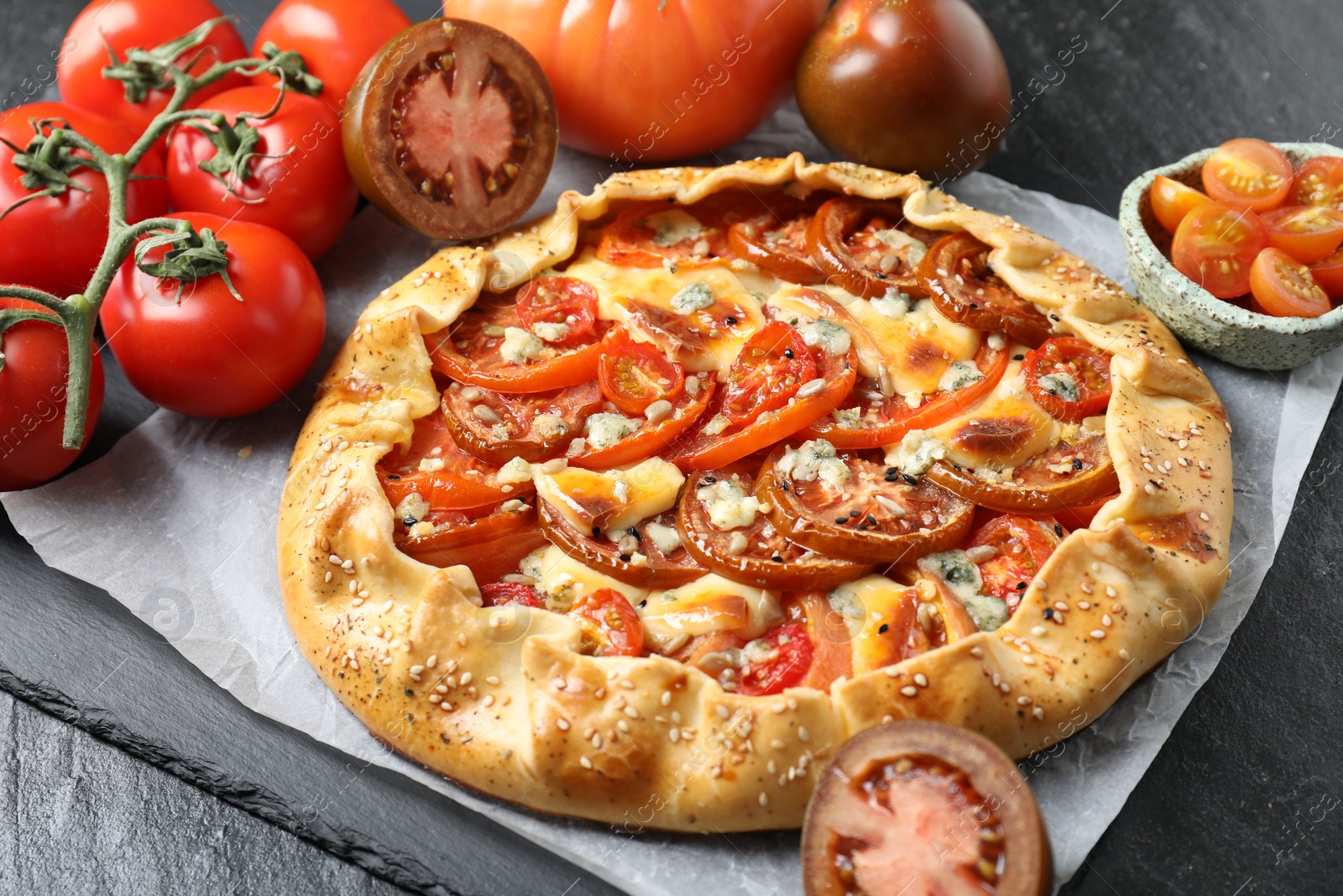 Photo of Tasty galette with tomato and cheese (Caprese galette) on dark table, closeup