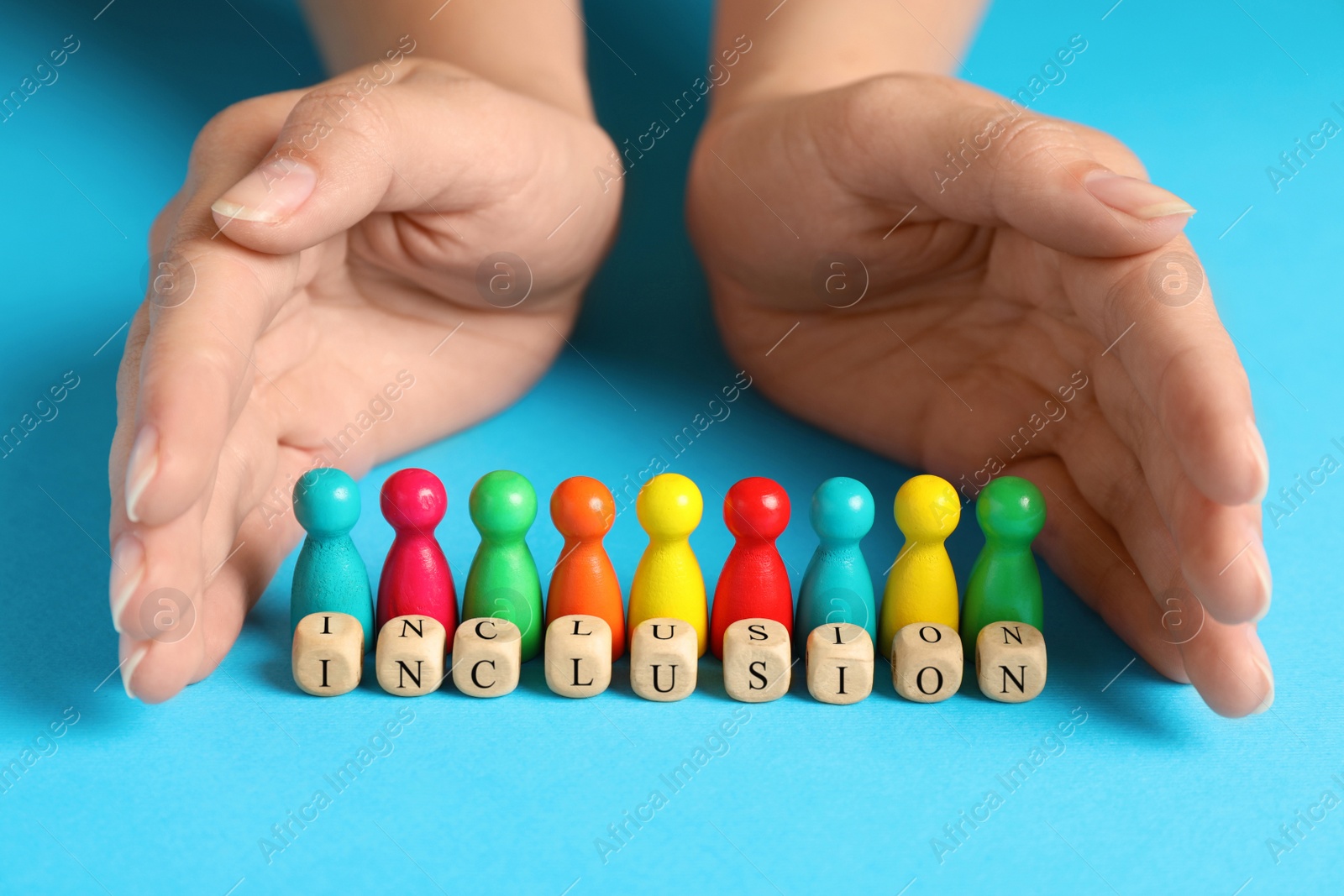 Photo of Woman protecting colorful pawns and wooden cubes with word Inclusion on turquoise background, closeup