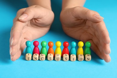 Photo of Woman protecting colorful pawns and wooden cubes with word Inclusion on turquoise background, closeup