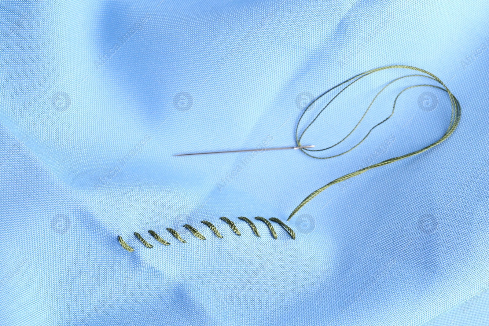 Photo of Sewing needle with thread and stitches on light blue cloth, above view