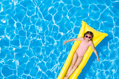 Cute little girl with inflatable mattress in swimming pool, top view. Space for text 