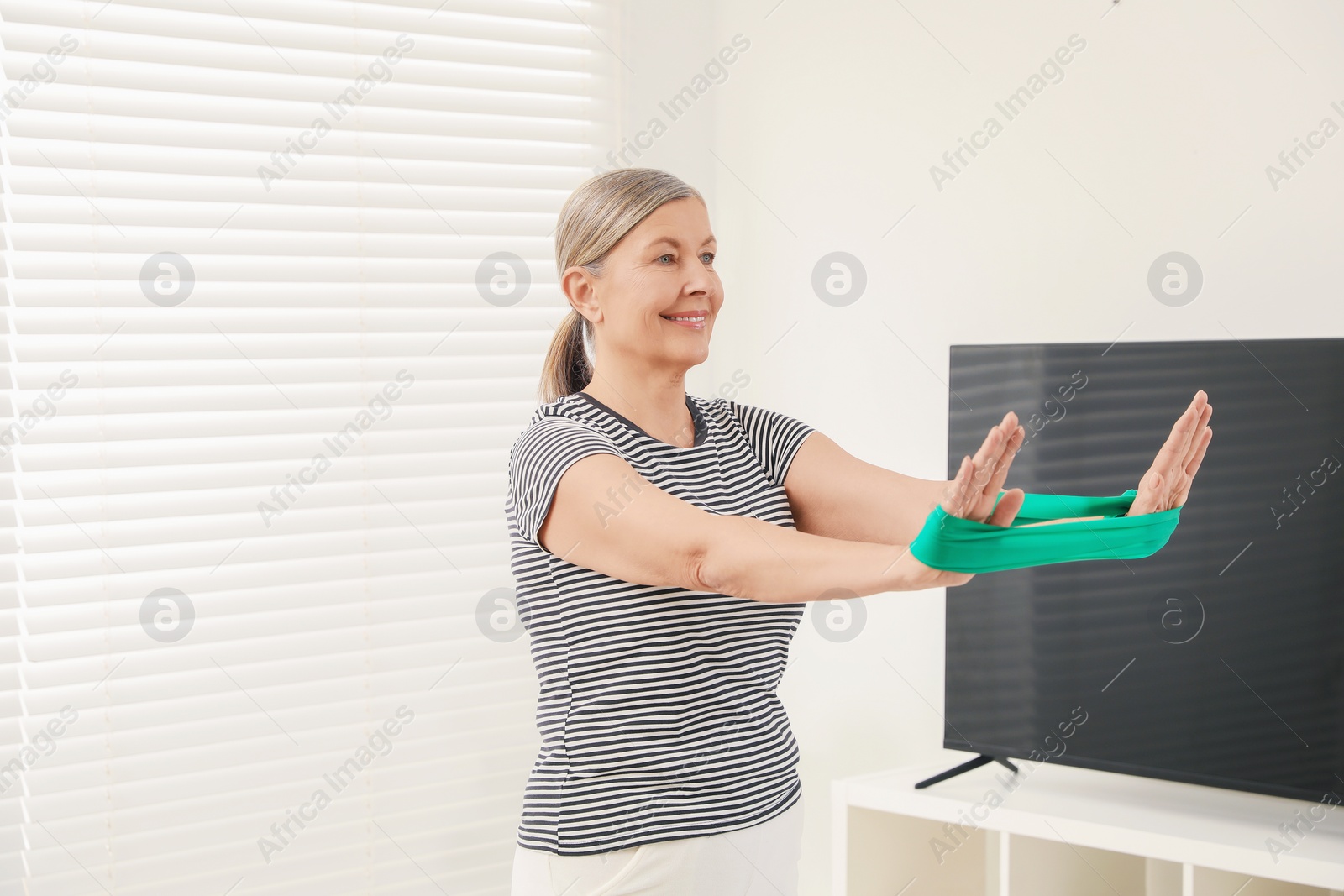 Photo of Senior woman doing exercise with fitness elastic band at home