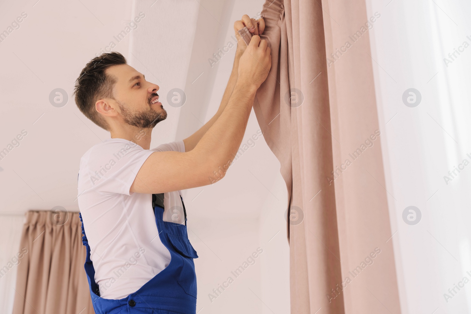 Photo of Worker in uniform hanging window curtain indoors