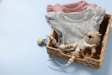 Photo of Different baby accessories and clothes in wicker box on light blue background, space for text
