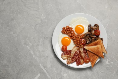 Photo of Plate of fried eggs, mushrooms, beans, tomatoes, bacon and toasts on grey table, top view with space for text. Traditional English breakfast