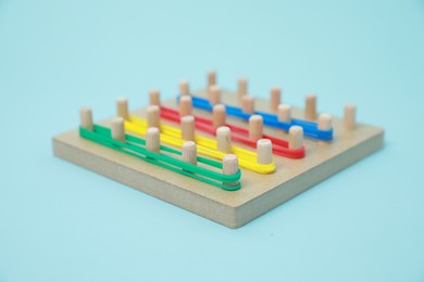 Photo of Wooden geoboard with rubber bands on light blue background. Educational toy for motor skills development