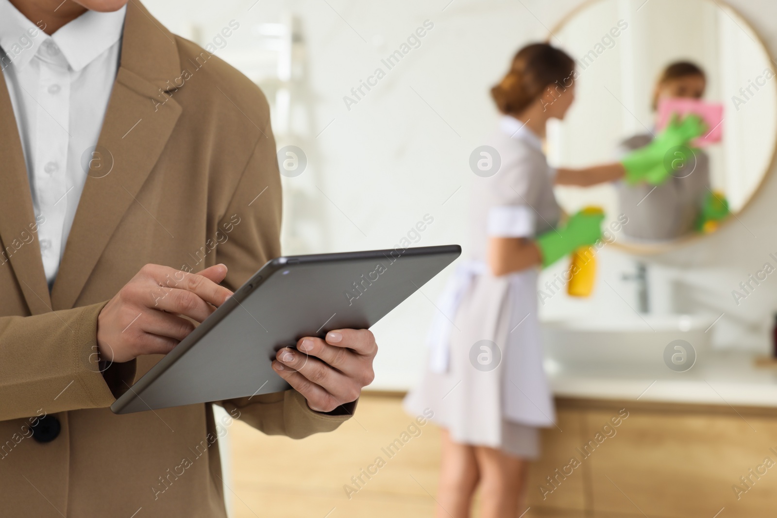 Photo of Housekeeping manager with tablet checking maid's work in hotel bathroom, closeup