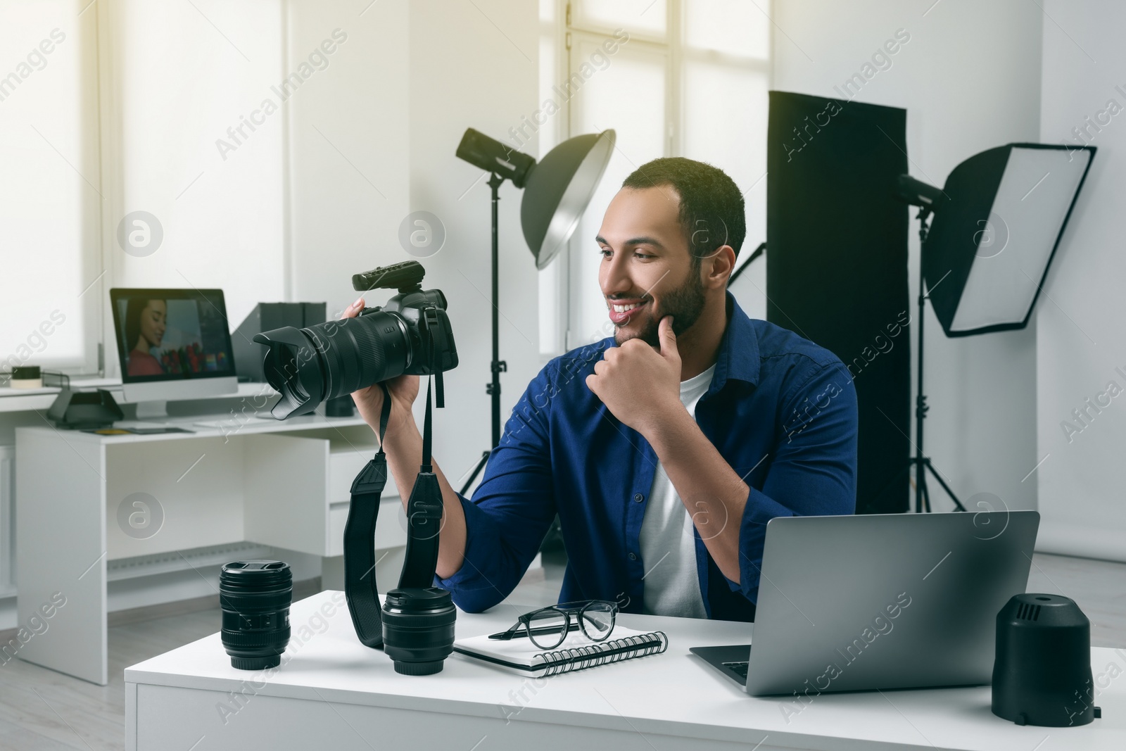 Photo of Young professional photographer with camera at table in modern photo studio