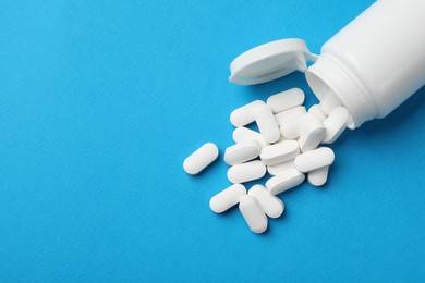 Photo of Vitamin pills and bottle on light blue background, top view. Space for text