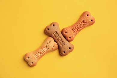 Photo of Bone shaped dog cookies on yellow background, flat lay