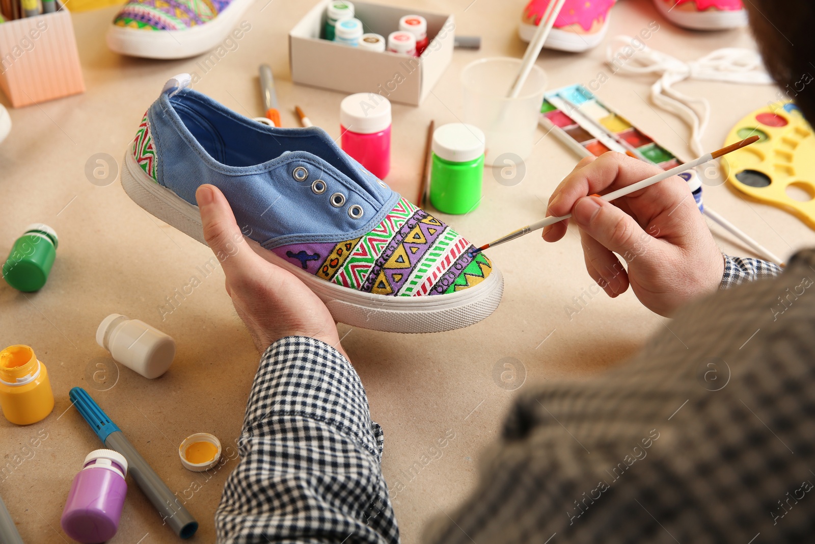 Photo of Man painting on sneaker at table, closeup. Customized shoes