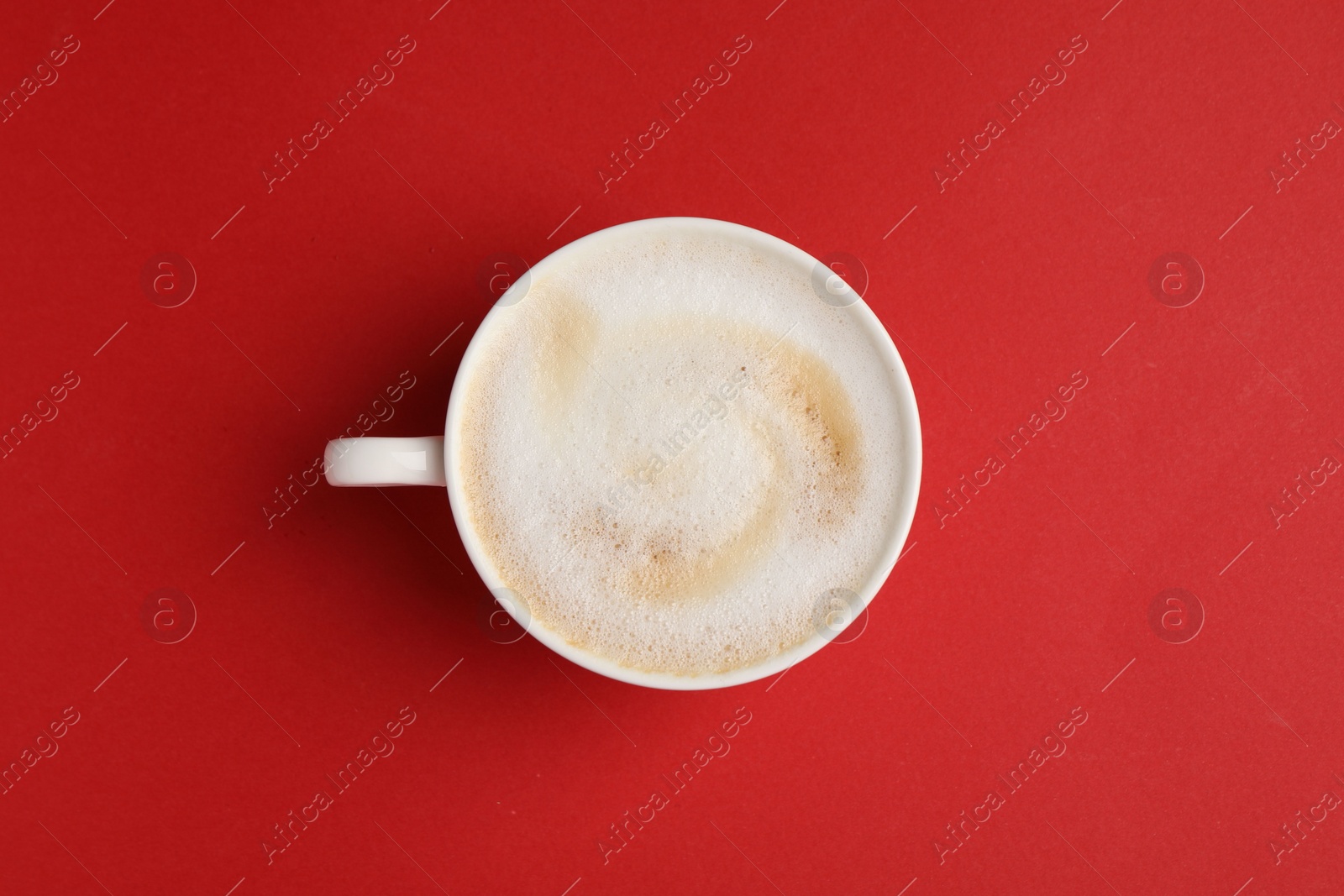 Photo of Tasty cappuccino in coffee cup on red background, top view