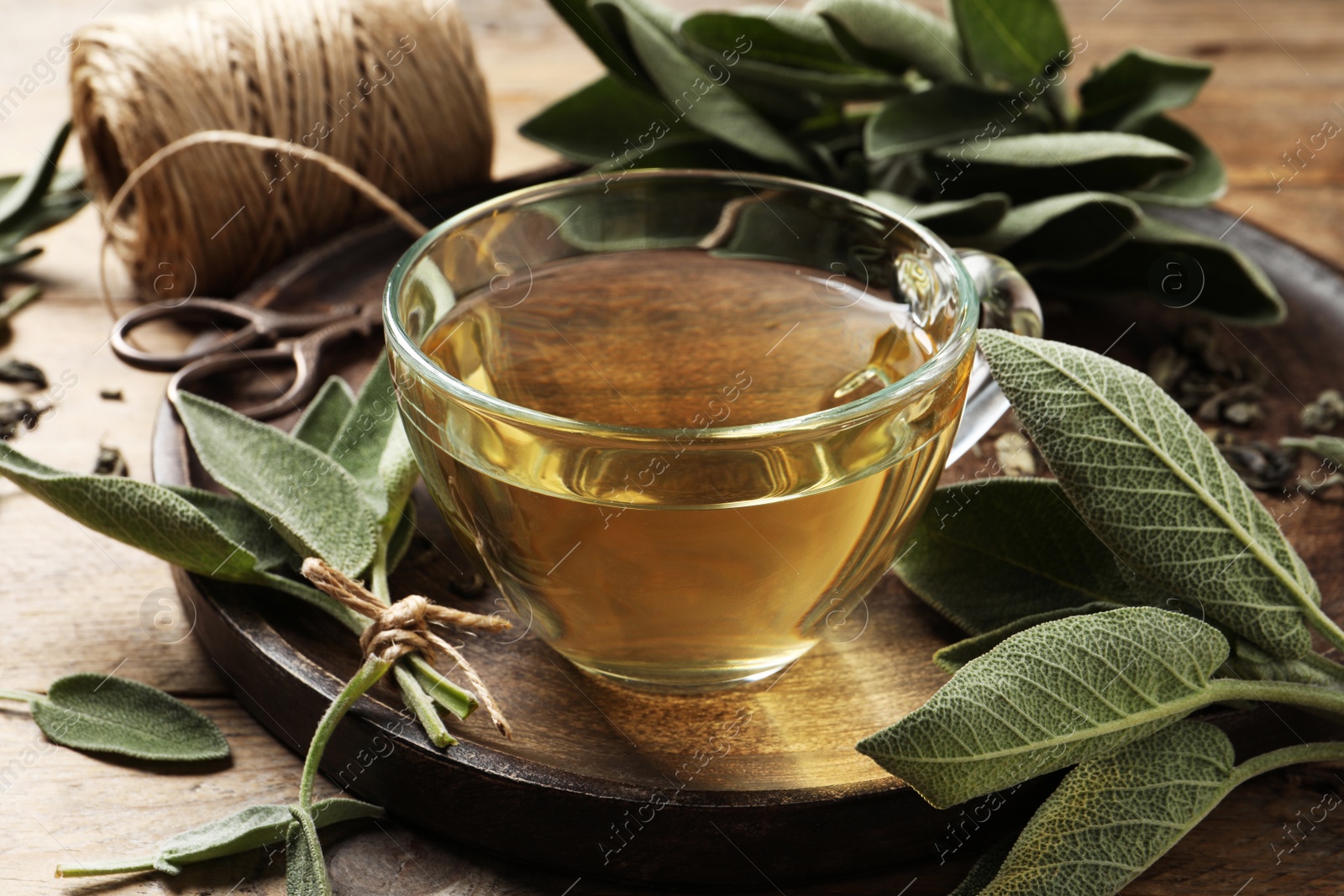 Photo of Cup of sage tea and green leaves on wooden tray