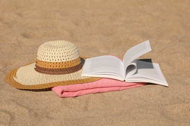 Open book, hat and pink towel on sandy beach
