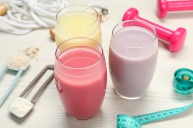 Photo of Tasty shakes, sports equipment, measuring tape and different powders on wooden table, closeup. Weight loss