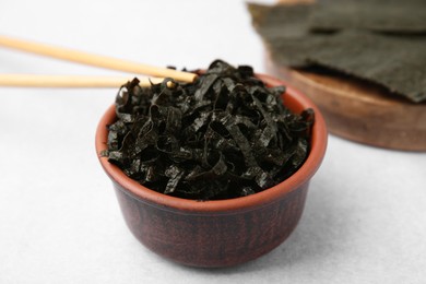 Photo of Bowl with chopped nori sheets and chopsticks on white table, closeup