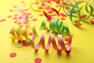 Photo of Colorful serpentine streamers and confetti on yellow background