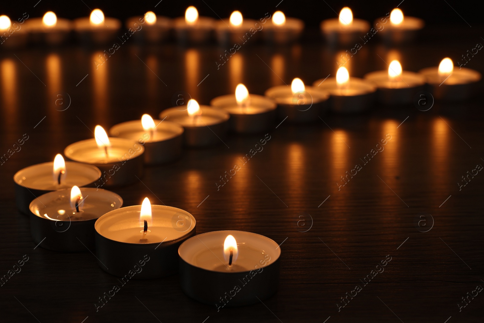 Photo of Burning candles on wooden table in darkness, closeup